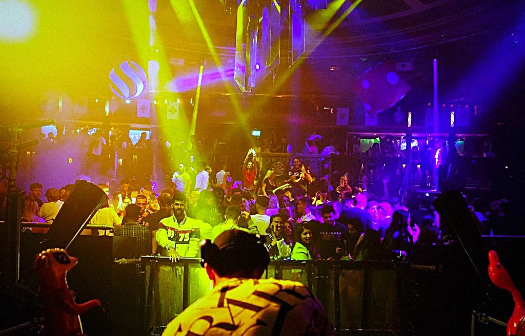 A packed dance floor under magenta and blue lasers, hands up